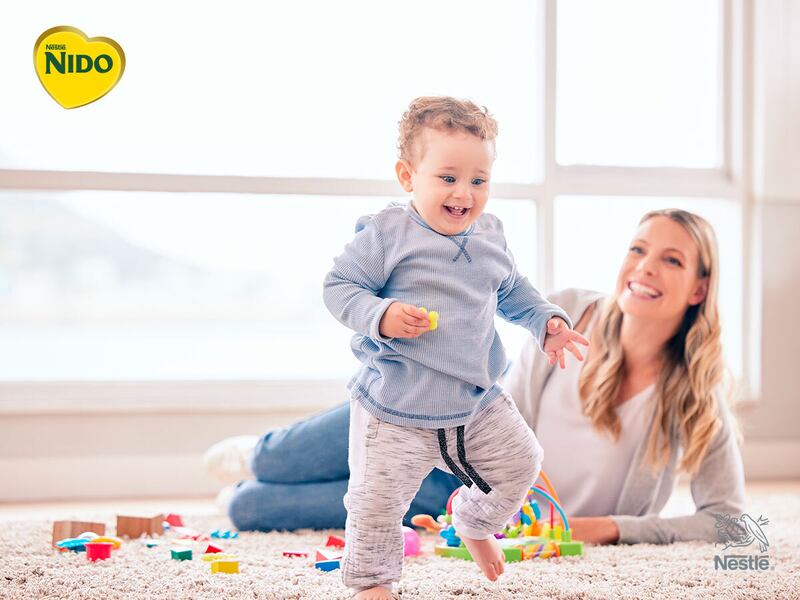 Mamá observa con cariño a su hijo pequeño mientras juega y da sus primeros pasos dentro de casa.