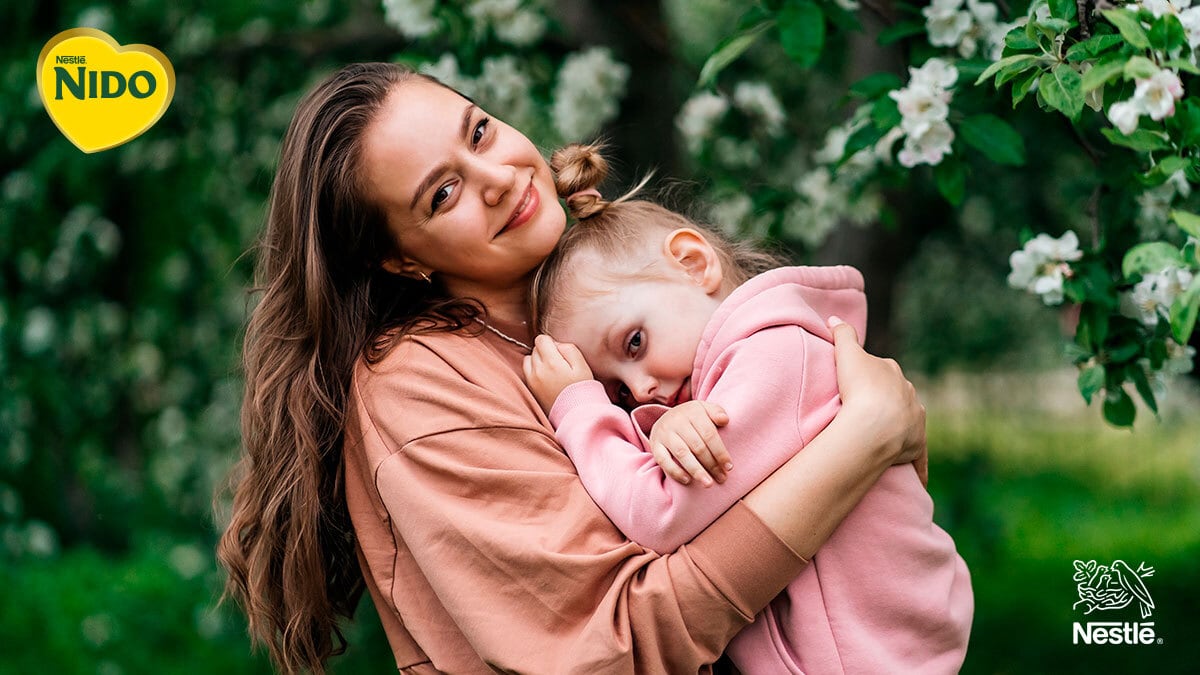Mamá abraza a su hija pequeña en un momento de cariño y conexión emocional al aire libre.