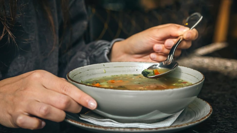 Una mujer en un café come una sopa de verduras baja en calorías