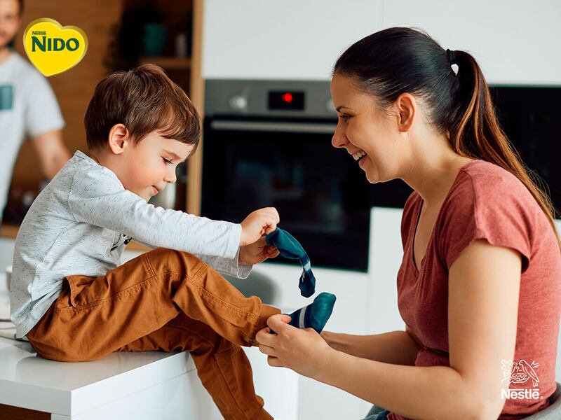 Mamá ayuda a su hijo a ponerse los calcetines mientras comparten un momento cotidiano en la cocina de su casa.